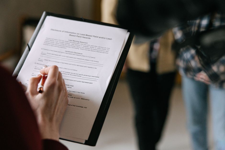 A person reviews a printed rental lease agreement with a pen on a kitchen table.